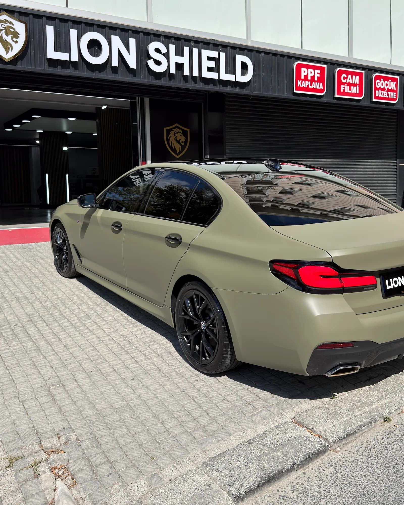 Mat haki BMW 5 Serisi’nin cam filmi uygulanmış yan ve arka camları, arkada uygulama merkezinin tabelası