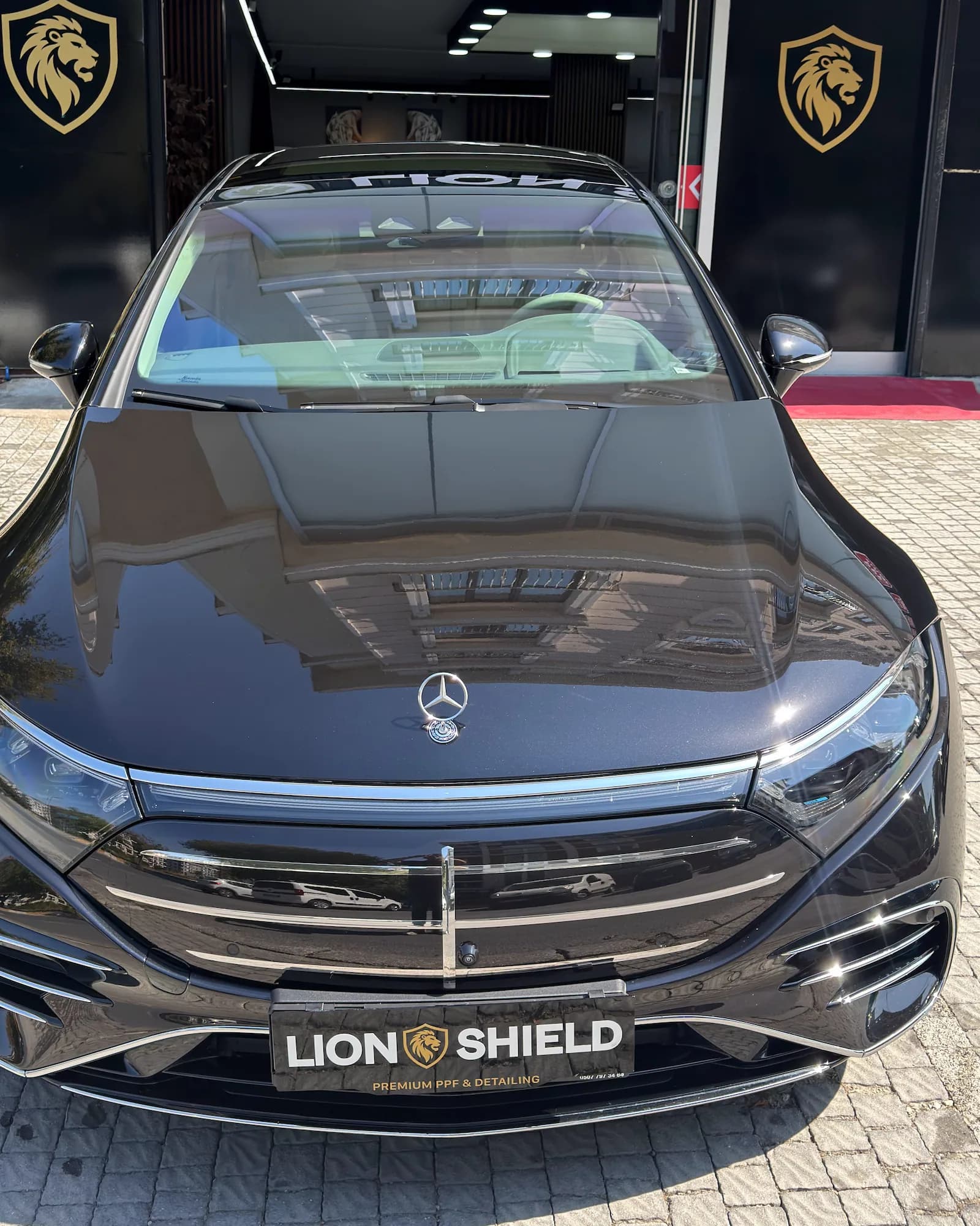Uygulama merkezinin önünde siyah Mercedes-Benz, kaputunda binaların yansıması