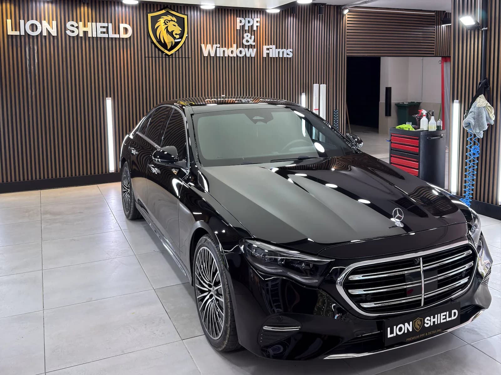 Uygulama merkezinde siyah Mercedes-Benz sedan, kaputunda tavan ışıklarının yansıması