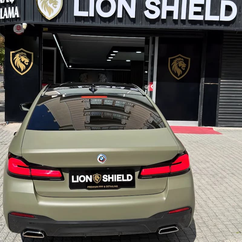 Uygulama merkezinin girişinde mat haki BMW 5 Serisi’nin arkadan görünümü